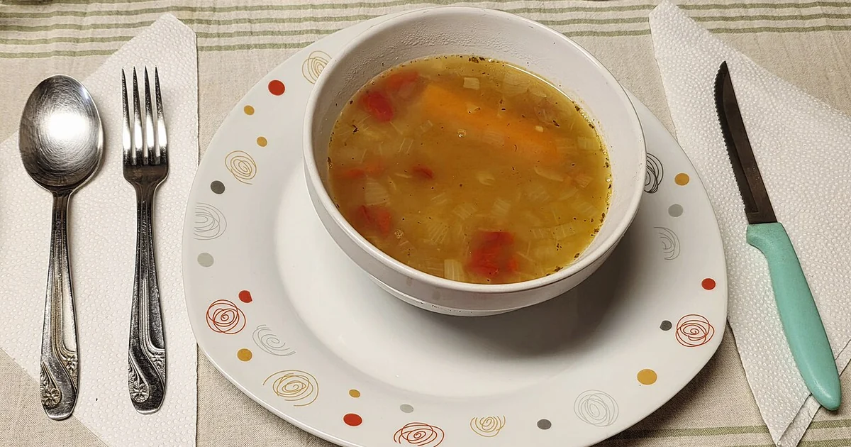 Homemade Argentine vegetable soup served hot in a white bowl, prepared with a light golden broth and chopped vegetables, including red bell pepper, onion, and potato. A simple and comforting home-style dish, photographed ready to eat at a d